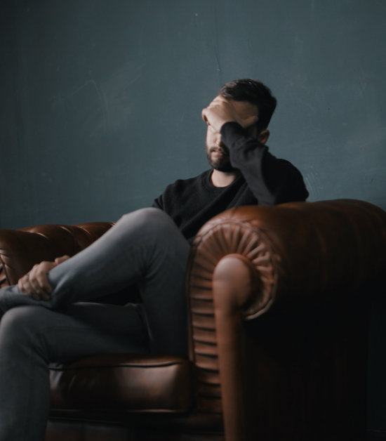 Photo of a man sitting on a sofa hold his head in one hand